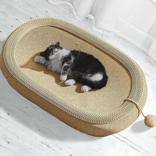 Chat noir et blanc endormi dans un large griffoir tressé beige avec balle en corde, sur sol en bois blanc.