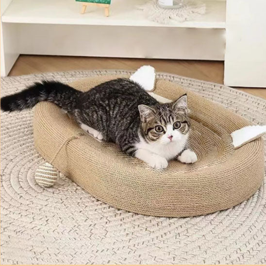 Chat tigré allongé dans un tapis griffoir ovale en corde, oreilles en tissu blanc et balle suspendue.
