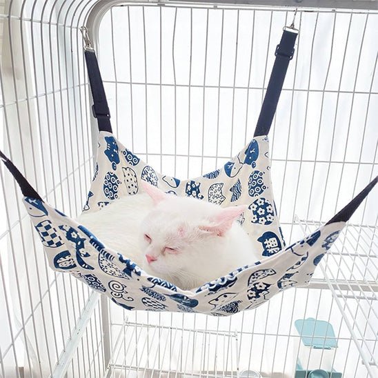 Chat blanc couché dans un hamac pour chat suspendu en tissu noir et blanc avec intérieur polaire, accroché dans une cage métallique