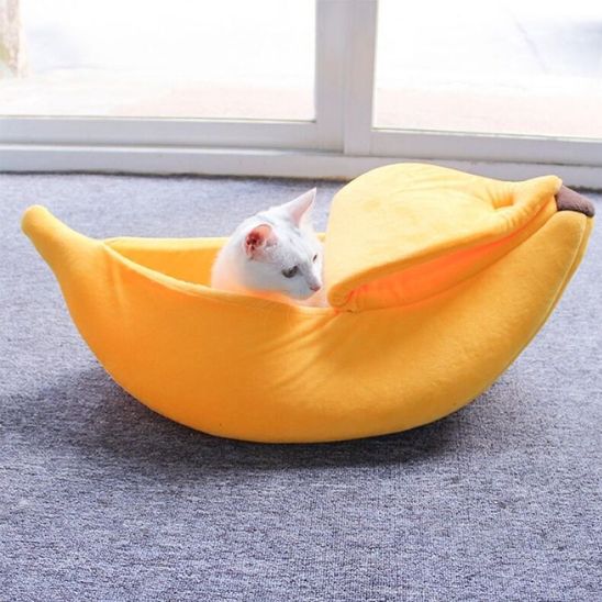 Niche pour chat en forme de banane moelleuse, avec un chat blanc confortablement installĂ© Ă lâintĂ©rieur