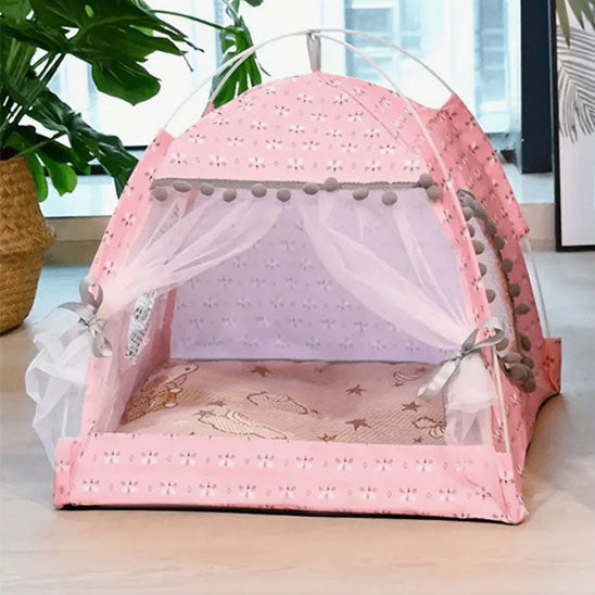 Tente pour chat rose au charme élégant avec pompons gris, coussin décoré et voilage blanc noué.