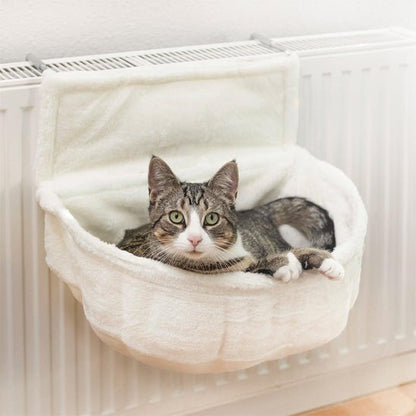 Chat blanc et gris détendu dans un hamac pour chat suspendu, fixé à un radiateur blanc