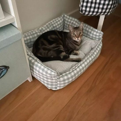 Lit pour chat vert clair avec un chat tigré couché à l’intérieur, posé sur un sol en bois